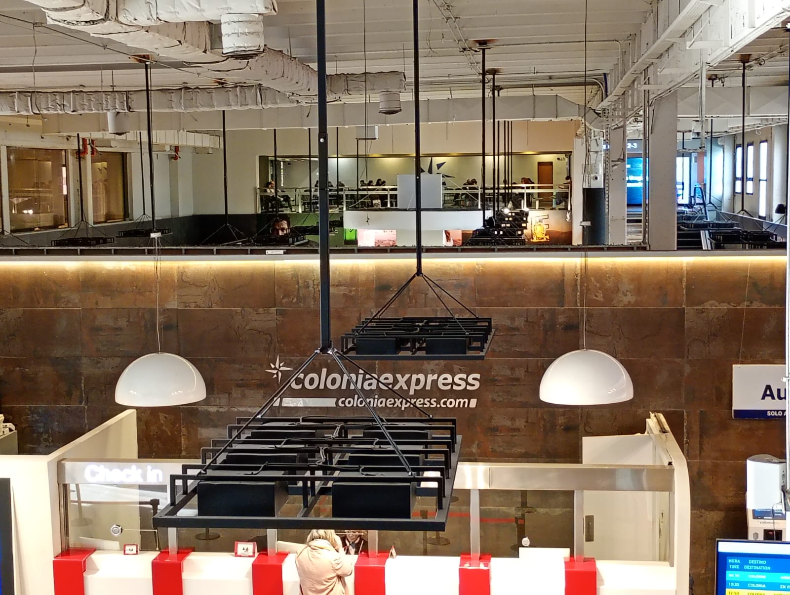 Área de check-in con señalética Colonia Express y pantallas de horarios
