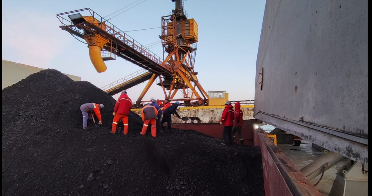 Personal técnico supervisando la carga de carbón junto a equipos de trasiego