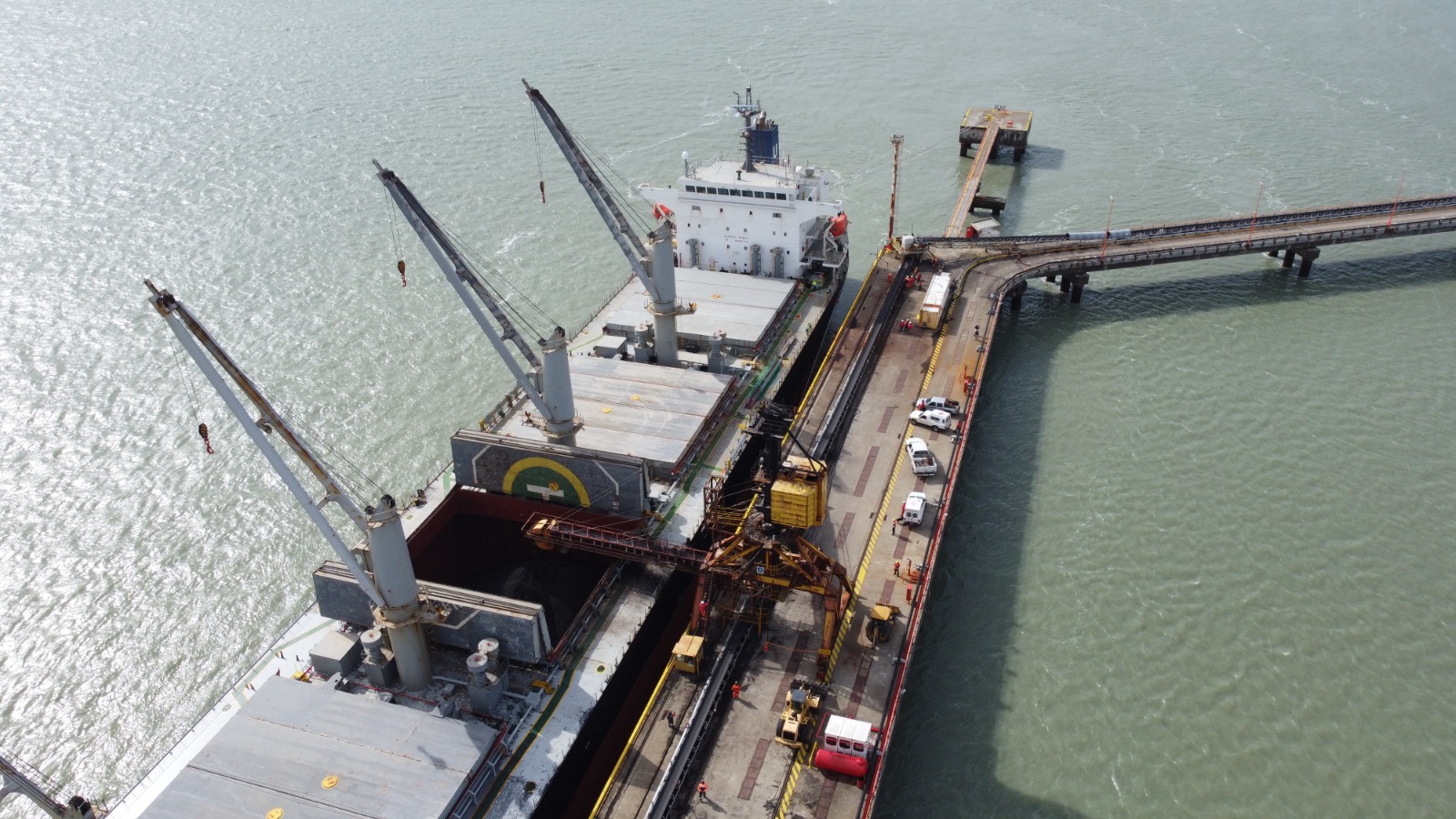 Vista aérea de carga a granel con grúas de cubierta y cargador móvil en el muelle